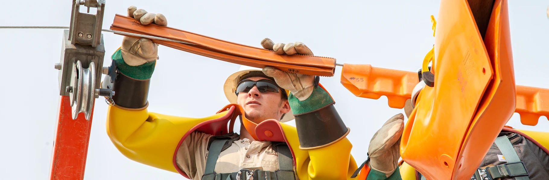 A utility worker in safety gear and gloves installs protective equipment on overhead electrical wires.