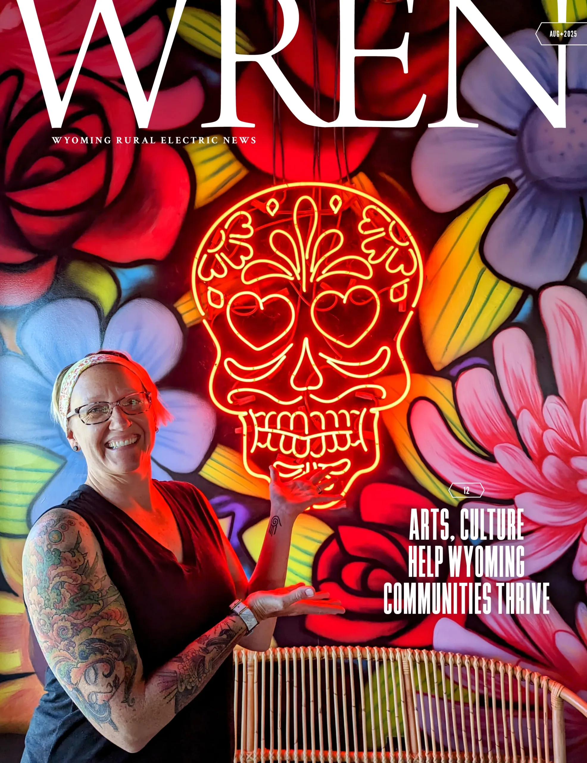 WREN 08-August 2025 Cover A smiling tattooed woman points at a glowing neon skull sign, standing in front of a colorful mural. The magazine cover reads, Arts, Culture Help Wyoming Communities Thrive.